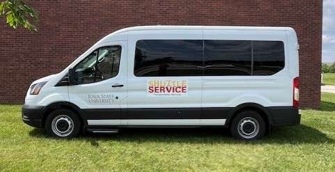 Tall white 15 passenger van with dark windows. The driver's door reads Iowa State University, and a decal in cardinal and gold reads Shuttle Service, Transportation Services.